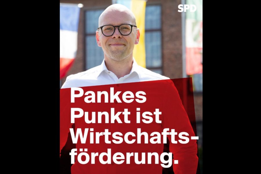 Bürgermeisterkandidat Simon Panke steht vor dem Rathaus. Auf de Bild steht "Pankes Punkt ist Wirtschaftsförderung."